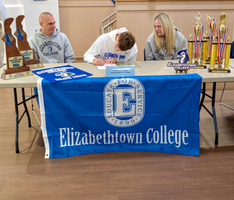 Sussex Academy senior Chase Ballinger signs his letter of intent to play soccer for Elizabethtown as his mom Christy and dad Jeff look on. Notice the hardware framing the shot.