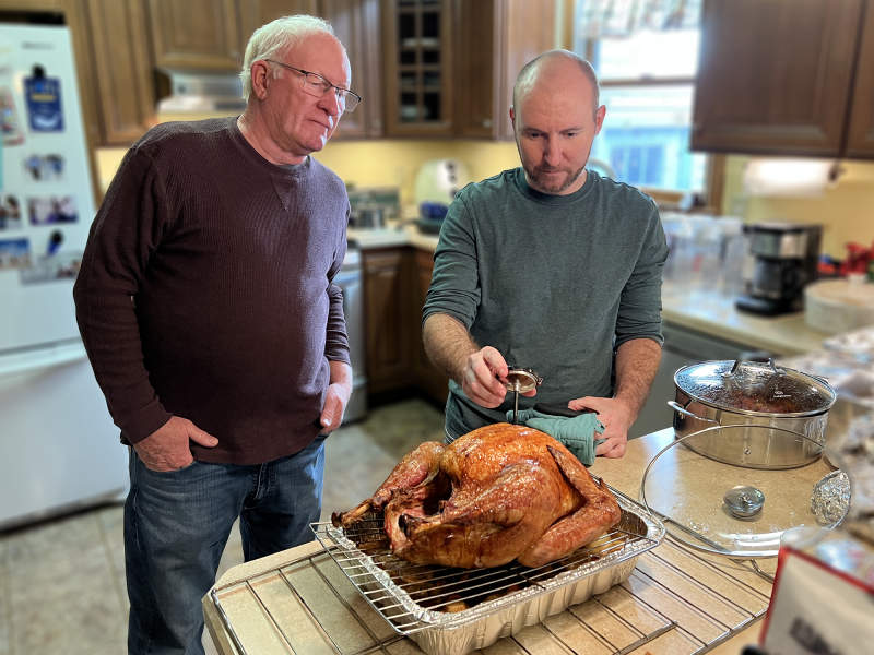 Thanksgiving chef Matt Young of Dover, right, checks the turkey’s temperature as his father Wayne looks on. PHOTO COURTESY OF KATIE YOUNG/UD