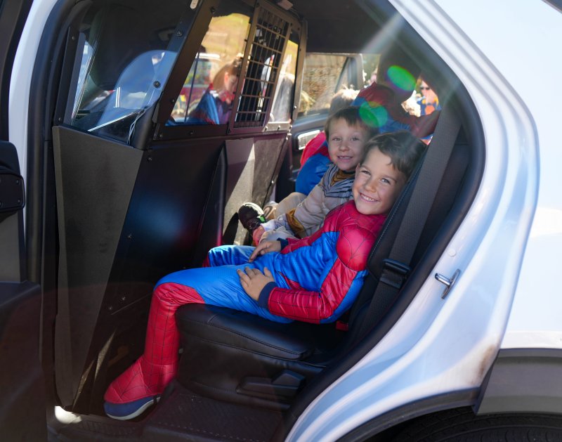 Spiderman gets arrested? Bryson Carmean sits in the back of a police car with Cooper Stevens to his right.
