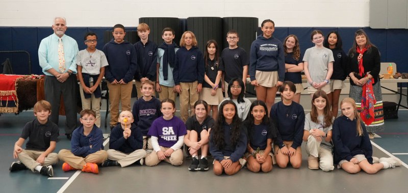 Boe Harris-Nakakakena, a member of the Turtle Mountain Chippewa and Spirit Lake Dakota tribal groups, standing back far right, visits with a Sussex Academy sixth-grade social studies class Nov. 13 for a hands-on educational presentation. Shown in back are (l-r) teacher Jon English; students Adrian Andrews, Kallen Hayes, Maverick Pine, Lucca Palmeri, Grant Hastings, Helena Olewiler, Jackson Sterner, Aialiyah Brunskill, Carmela Hudson, Mary Bowe and Mia Hendricks; and Harris-Nakakakena. In middle are Jace Hilderbrand and Bianca Carmella Benito. In front are Laurence Curry, Nash Dondarski, Ivan Lynn, Zoe Sexton, Alexsis Frantz-Andrie, Kay Samayoa-Gijalva, Kelly Samayoa-Gijalva, Marco LaRagione, Alessia Retzlaff and Maeve Sammons. ELLEN MCINTYRE PHOTOS