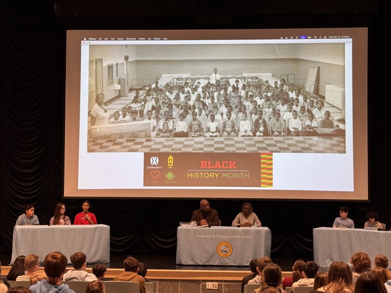 Frederick D. Thomas Middle School Junior Justice League students hosted longtime Cape district leaders Bill Collick and Janet Maull-Martin for a Black History Month presentation in Lewes. Gathered on stage are (l-r) Kennedy Dantzler, Emery Goldmeier, Rylee Freeman, guest speakers Collick and Maull-Martin, Oliver Sechler and Alexis Negron. Among the individuals pictured in the large group photo backdrop are Collick and Maull-Martin as young students and Principal Frederick D. Thomas, the late educator for whom the middle school is named. SUBMITTED PHOTO