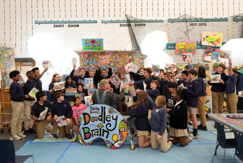 The students hold up their artwork for artist John Donato to see.