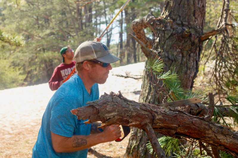Chuck Legates saws off a thick branch from a fallen tree limb.