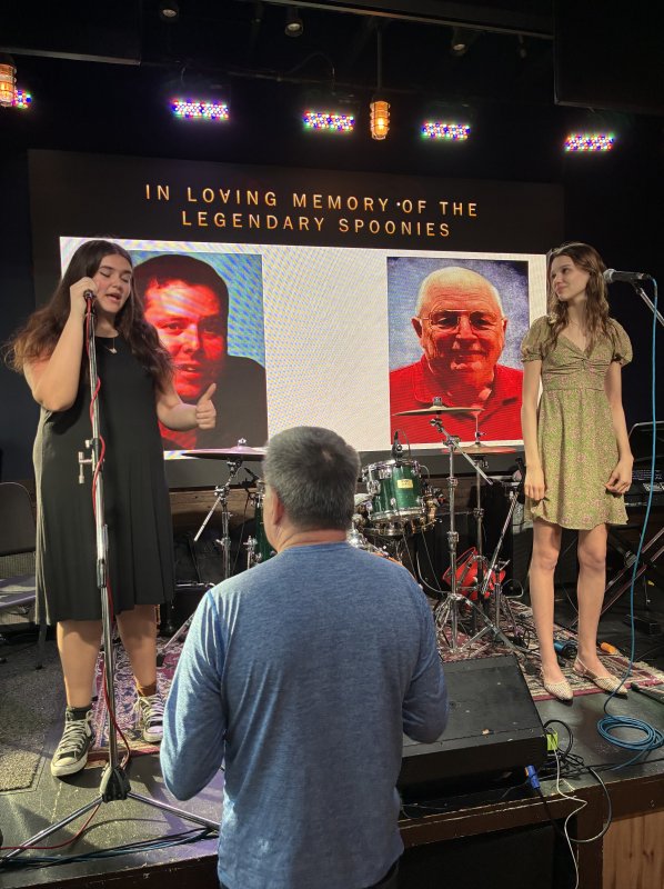 Cape High juniors and music program students Anna Currence, left, and Ruby Quinn share their talents with the audience. On the screen behind them are photos of Stephen “Spoonie” Sponaugle, left, and his late father, Bill “Spoonie” Sponaugle.