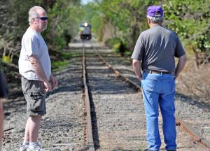 John Roberts of the Fort Miles Historic Association, left, and Joe Bargelski of Lewes wait on the tracks as the train hauling the gun barrel approaches in the distance. BY NICK ROTH