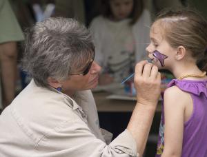 Starr Reynolds gets a purple dolphin face painting from Ellen Passman of the Milton Art Guild. BY DENY HOWETH