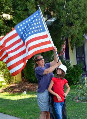 Lori and Kassidy Brown, who live along the parade route, wave a 48-star U.S. flag from the Korean War. BY RON MACARTHUR