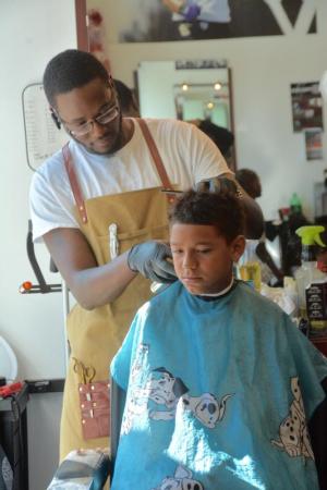 With light from the front window of the shop on them, barber John Glover styles the hair of William Harmon of Georgetown.