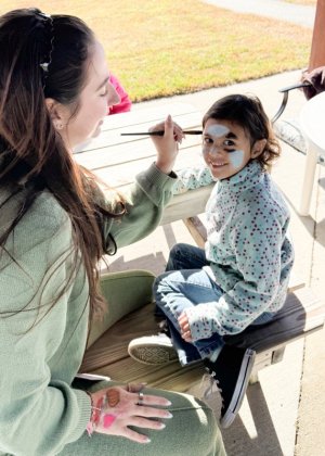 Little Vikings student Livia Castro De Sa, right, smiles as she has her face painted at a fall fest by Isabelle O’Donnell, school psychologist.